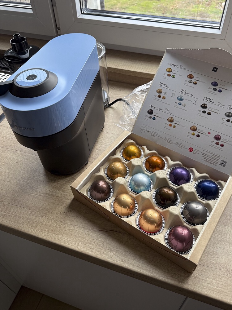 A capsule coffee machine next to a box of colourful coffee capsules