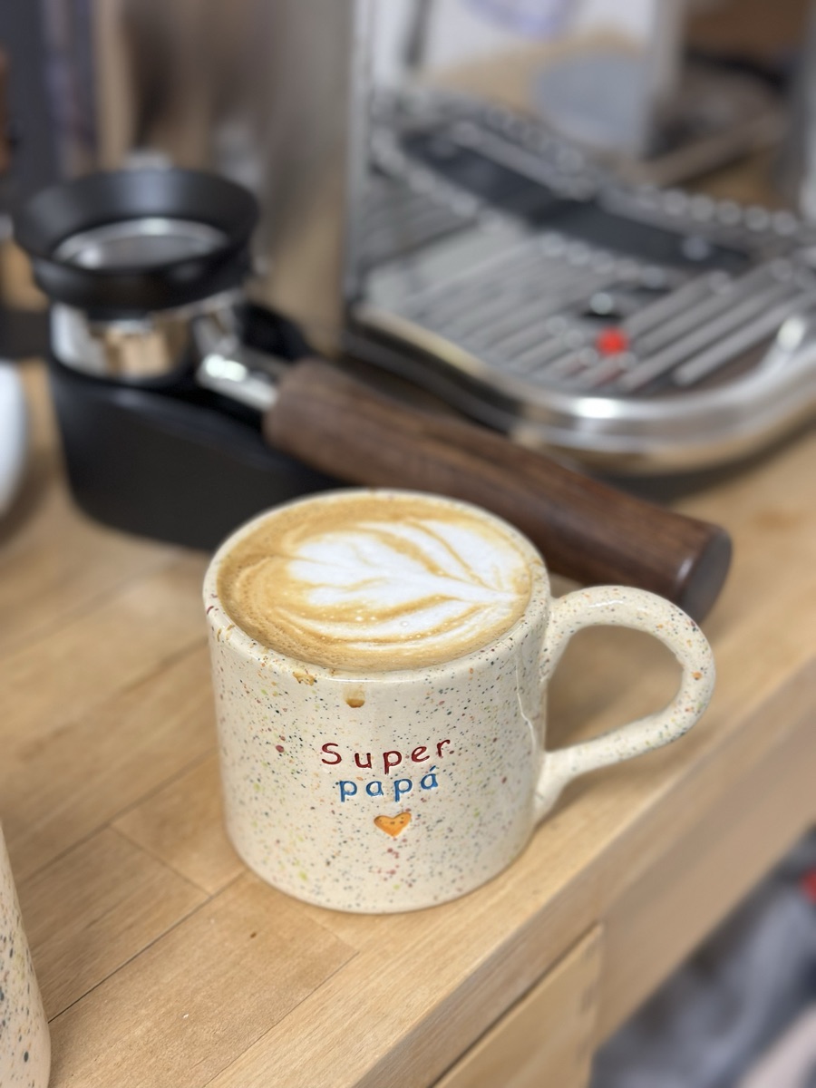 A tulip in latte art, in a speckled Super papá mug next to the espresso machine